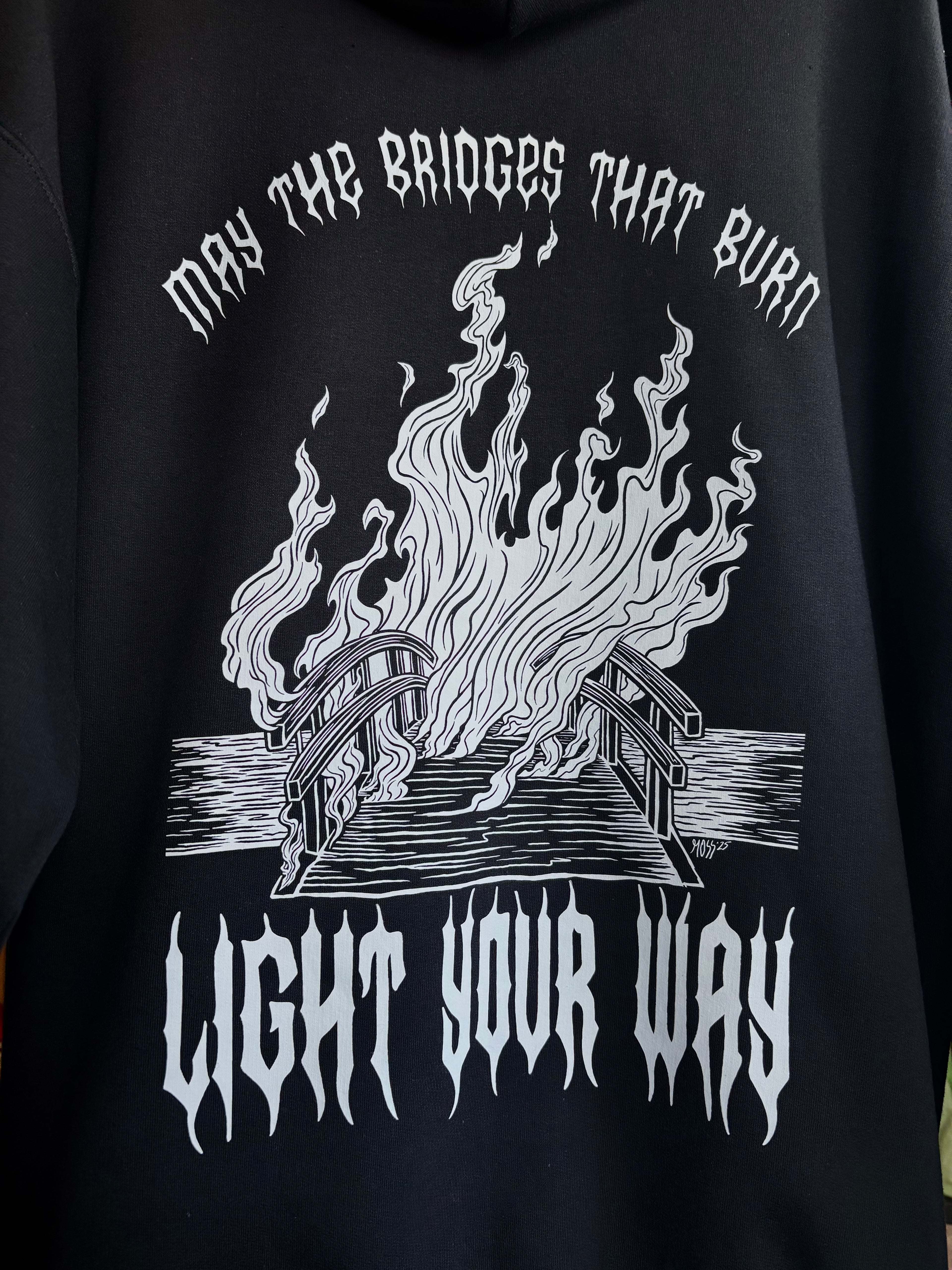 a closeup look at the full back print for the Burning Bridges design, showing a bridge covered in a wall of flames, surrounded by the text "MAY THE BRIDGES THAT BURN LIGHT YOUR WAY"