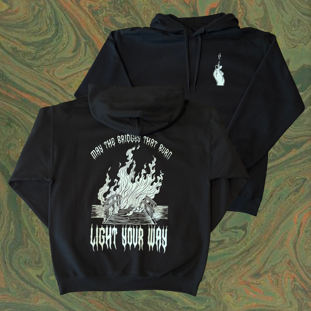 black hoodie with a burning bridge printed on the back, surrounded by the text "MAY THE BRIDGES THAT BURN LIGHT YOUR WAY." the front shows a hand holding a burnt match