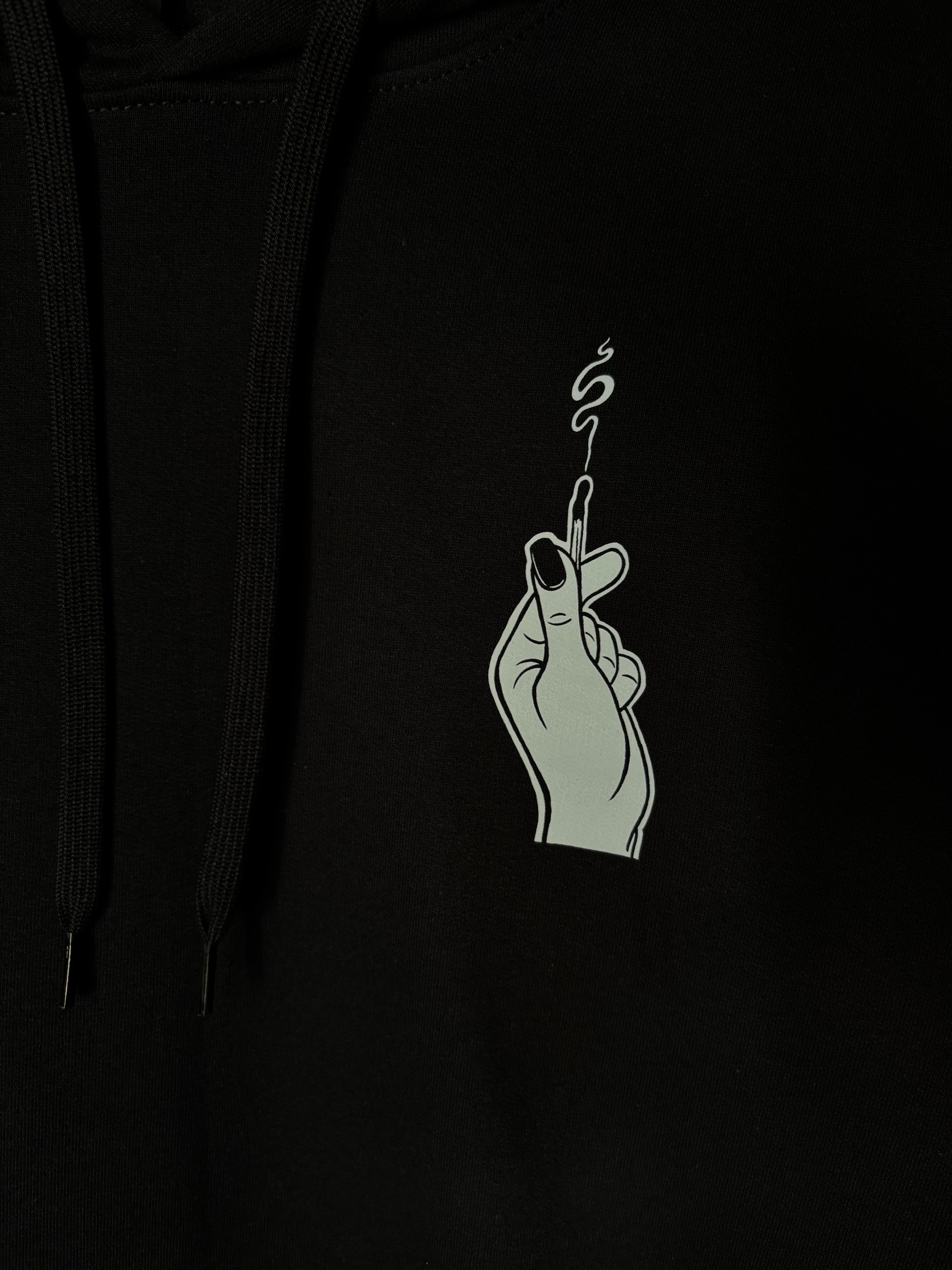 a closer look at the hand holding the burnt match, printed as a club patch on the front of a black hoodie
