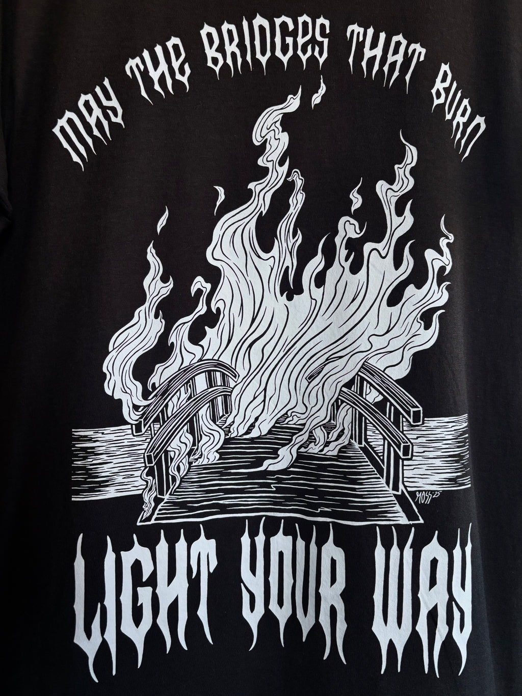 a closeup look at the full back print for the Burning Bridges design, showing a bridge covered in a wall of flames, surrounded by the text "MAY THE BRIDGES THAT BURN LIGHT YOUR WAY"