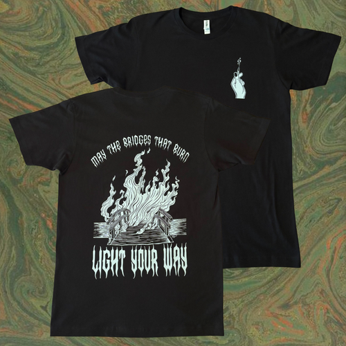 black t-shirt with a burning bridge printed on the back, surrounded by the text "MAY THE BRIDGES THAT BURN LIGHT YOUR WAY." the front shows a hand holding a burnt match