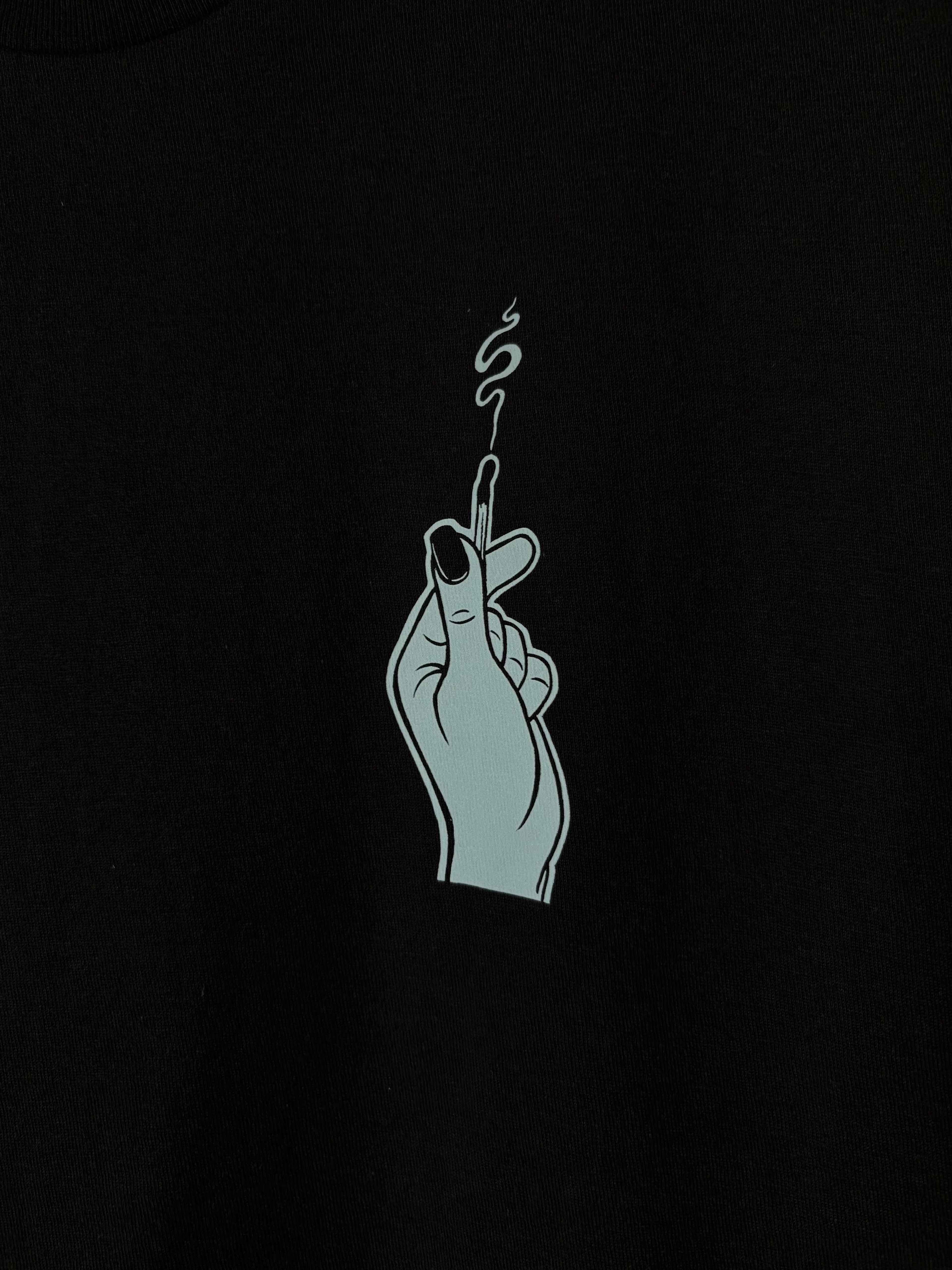 a closer look at the hand holding the burnt match, printed as a club patch on the front of a black t-shirt