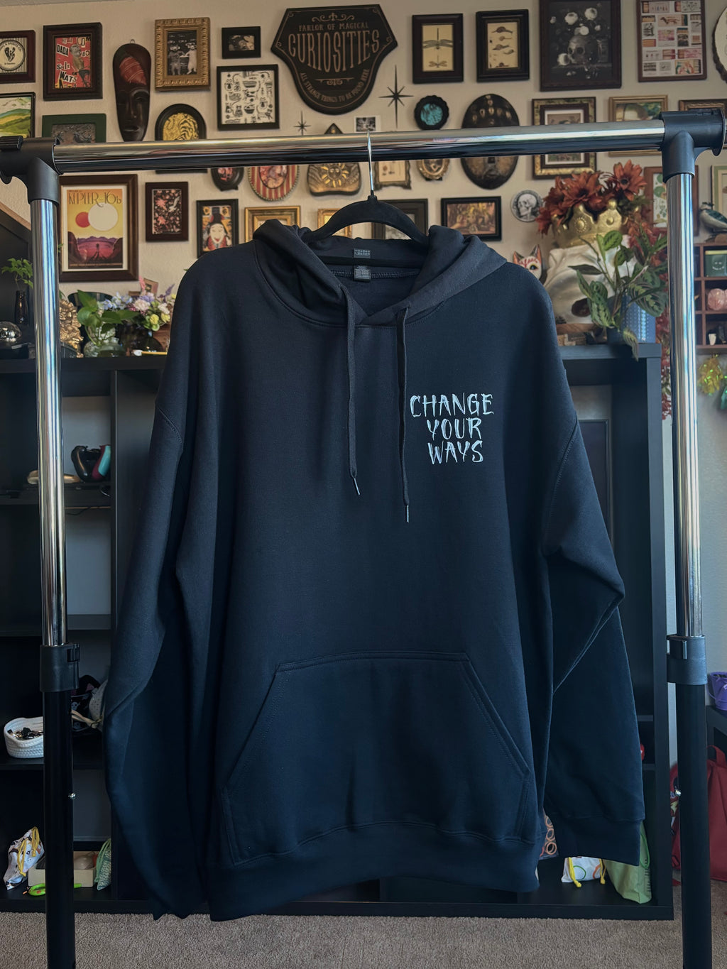 the Change Your Ways tarot inspired design printed on a black hoodie, hanging on a rack to show the front with a club patch print