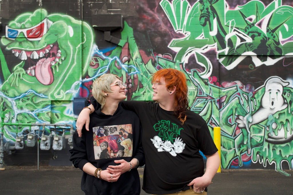 Two people standing in front of a colorful graffiti wall.