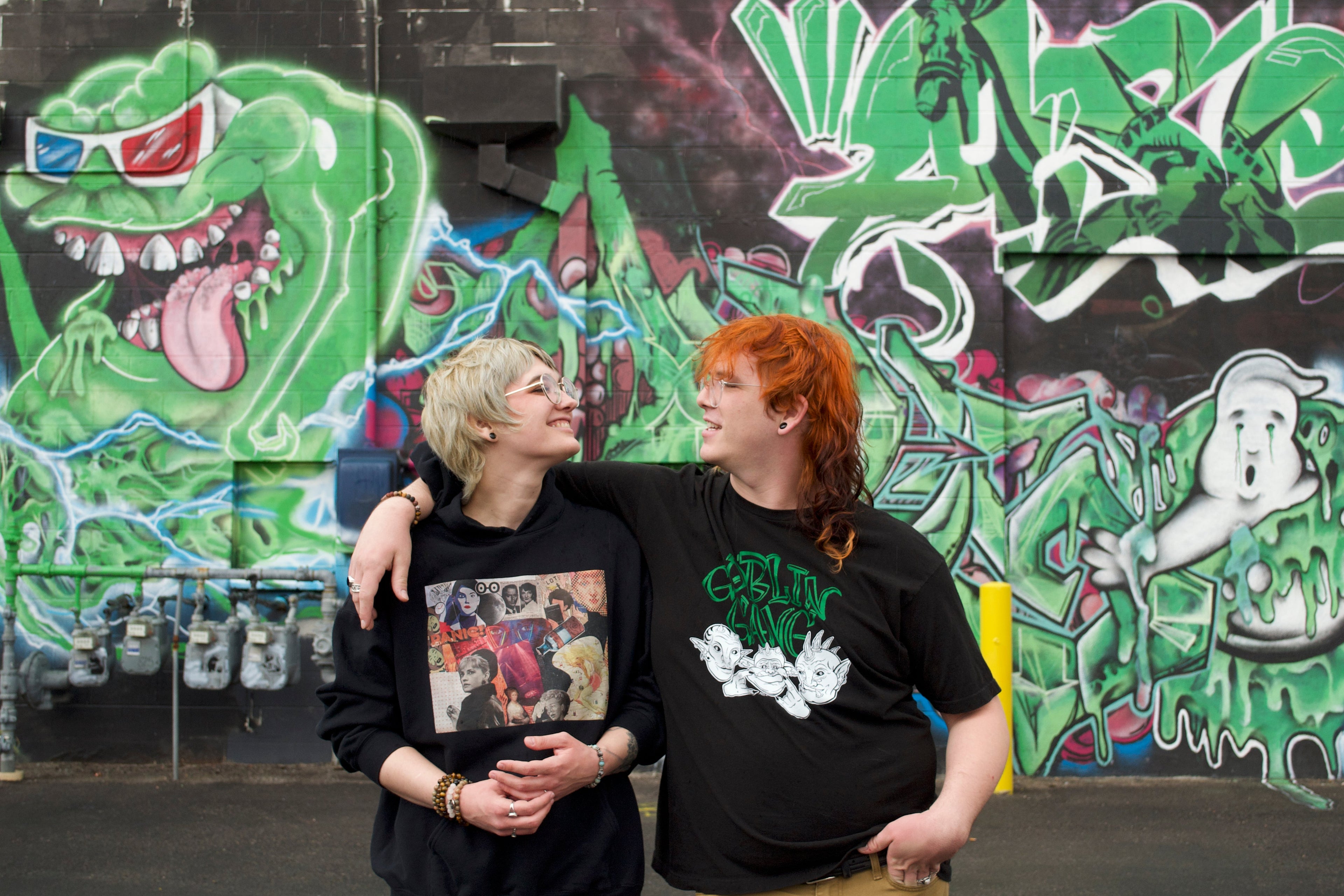 Two people standing in front of a colorful graffiti wall.