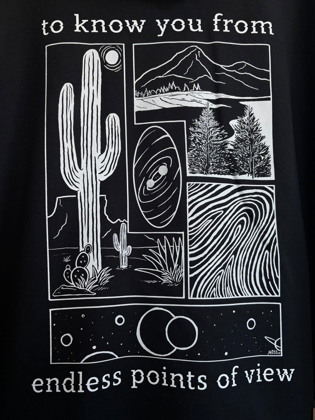 a closeup look at the full print on the back of a black hoodie, depicting an arrangement of a desert scene, a river flowing through a valley, a closeup of a finger print, and images of the cosmos. "to know you from endless points of view" is printed around the scenes