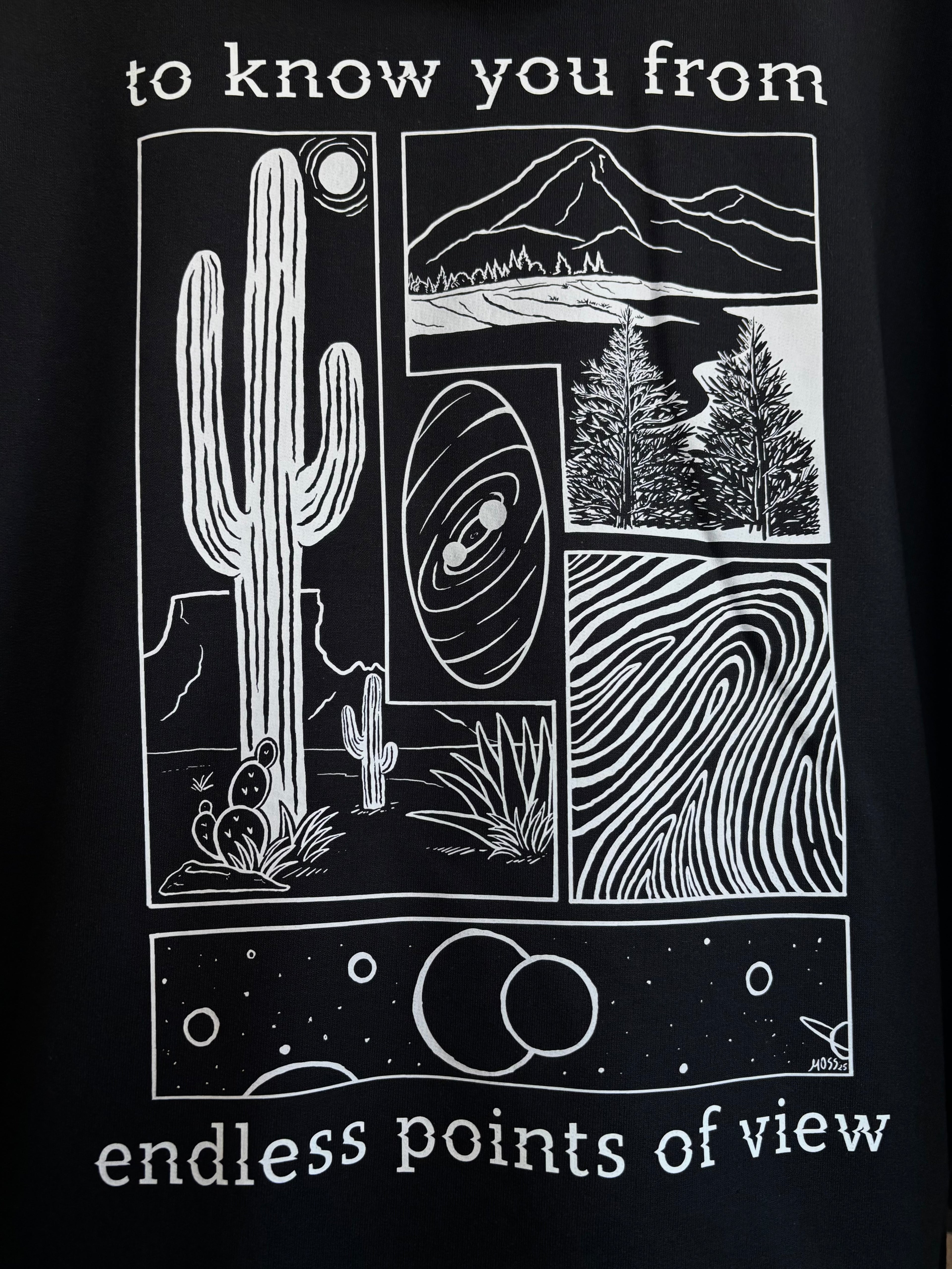 a closeup look at the full print on the back of a black hoodie, depicting an arrangement of a desert scene, a river flowing through a valley, a closeup of a finger print, and images of the cosmos. "to know you from endless points of view" is printed around the scenes