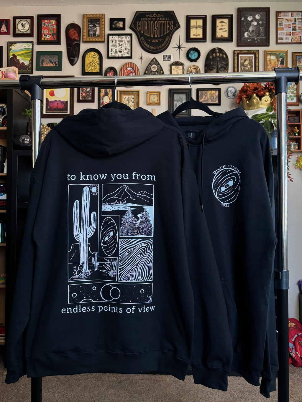 two black hoodies hanging on a rack to show the full back print and the front club patch for the Endless Points of View design