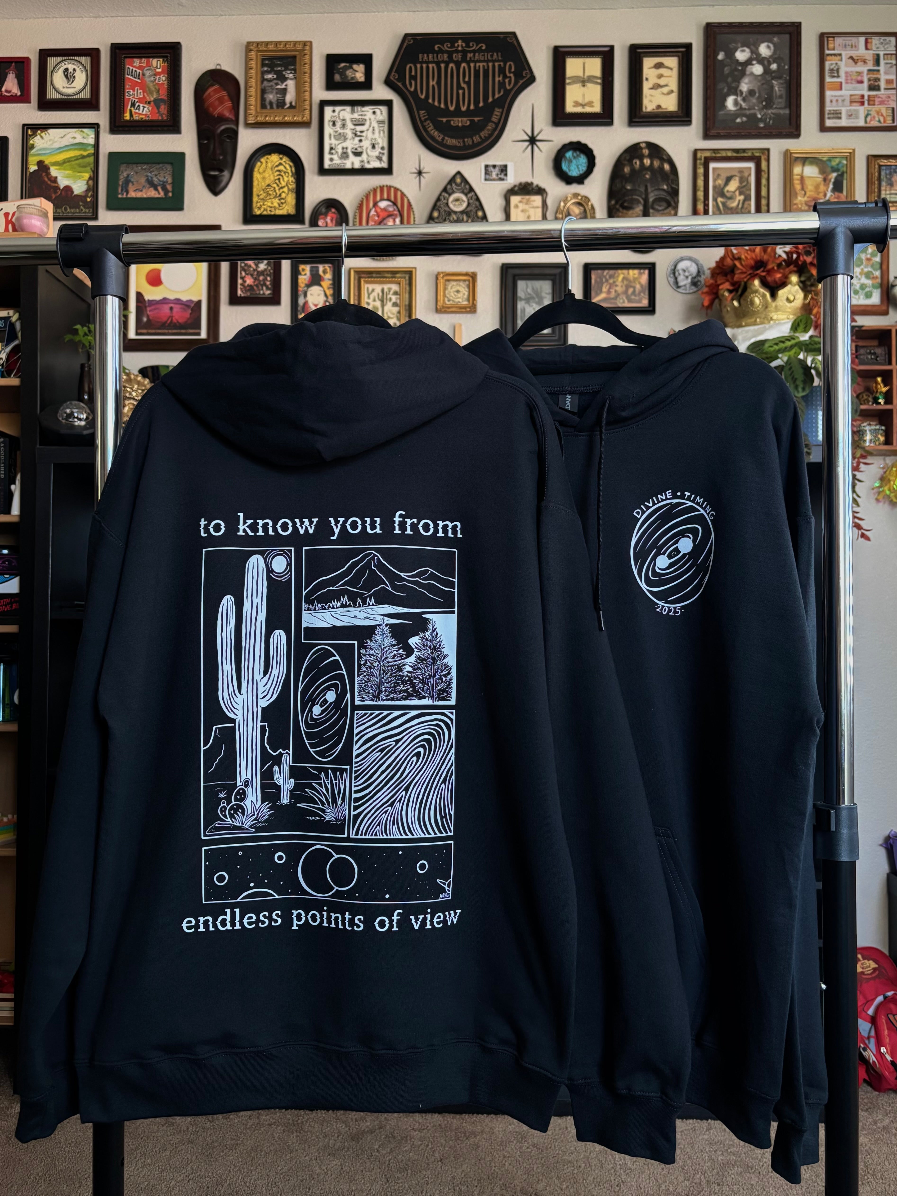 two black hoodies hanging on a rack to show the full back print and the front club patch for the Endless Points of View design