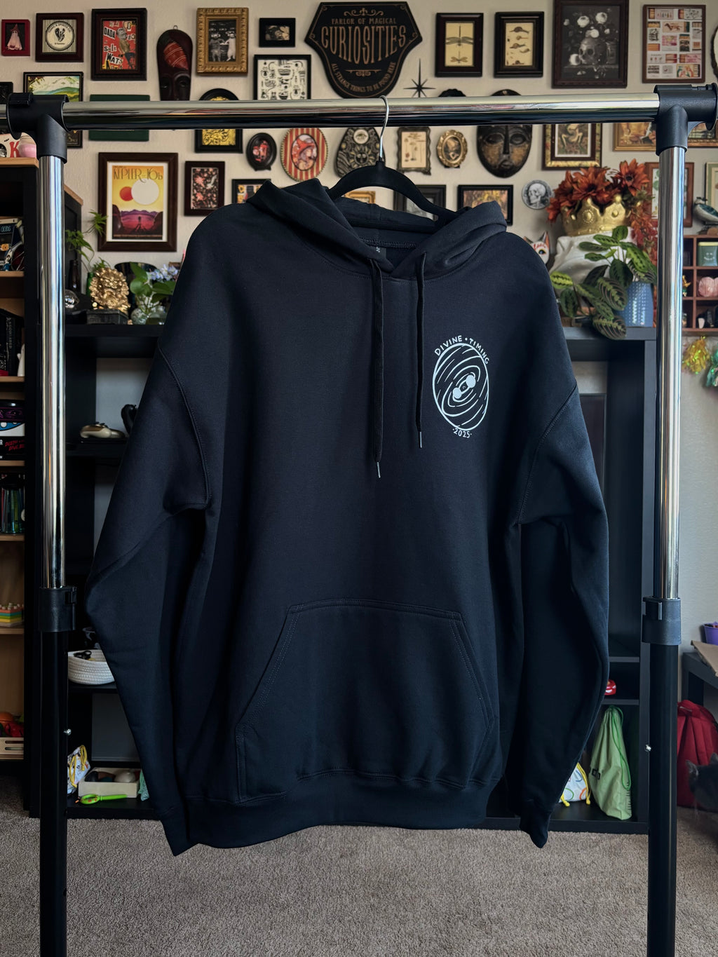 black hoodie hanging on a rack to show the front with the Divine Timing Binary Star badge printed as a club patch