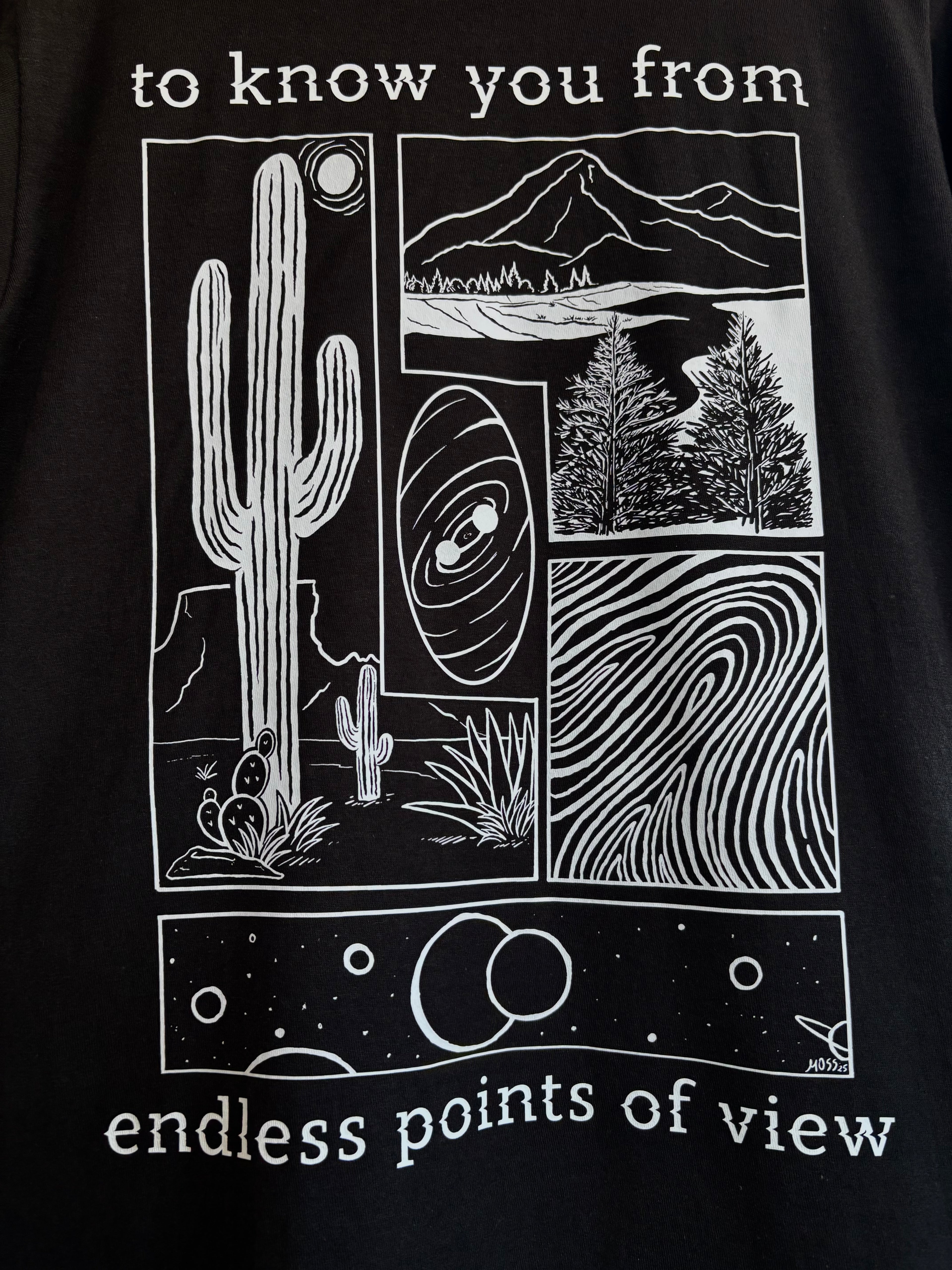 a closeup look at the full print on the back of a black t-shirt, depicting an arrangement of a desert scene, a river flowing through a valley, a closeup of a finger print, and images of the cosmos. "to know you from endless points of view" is printed around the scenes