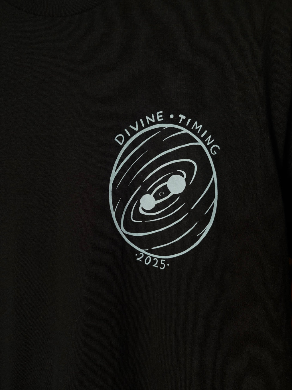closeup look at the Divine Timing Binary Star badge printed as a club patch on the front of a black t-shirt