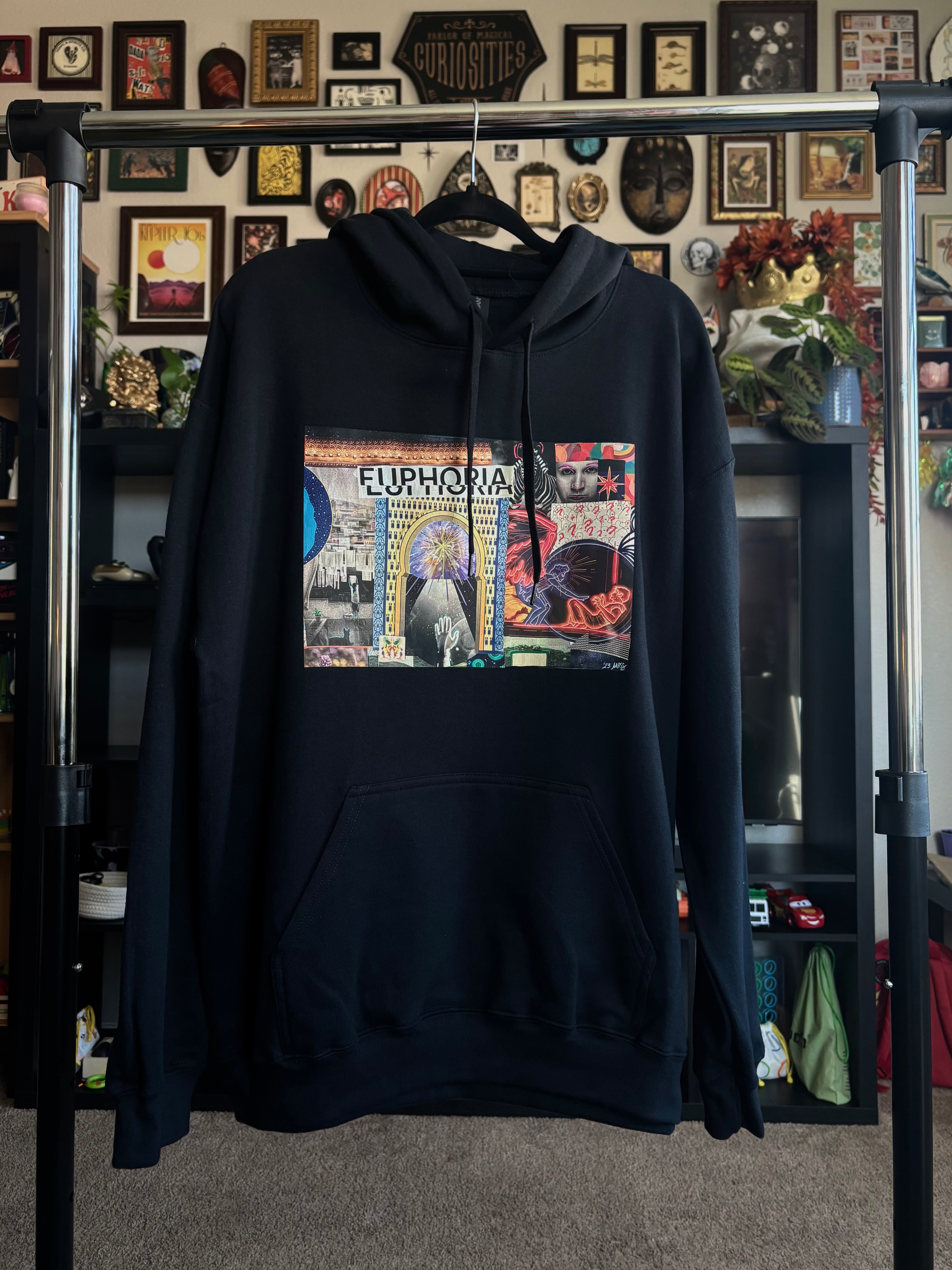black hoodie with a colorful graphic design of the EUPHORIA collage printed across the chest, hanging on a rack
