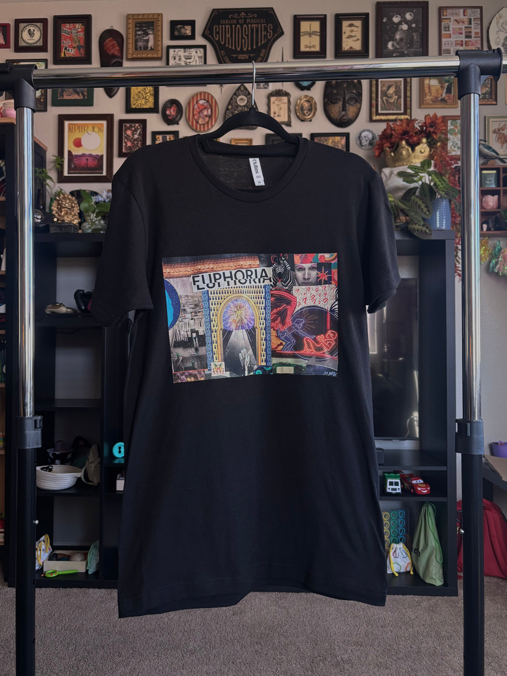 black t-shirt with a colorful graphic design of the EUPHORIA collage printed across the chest, hanging on a rack