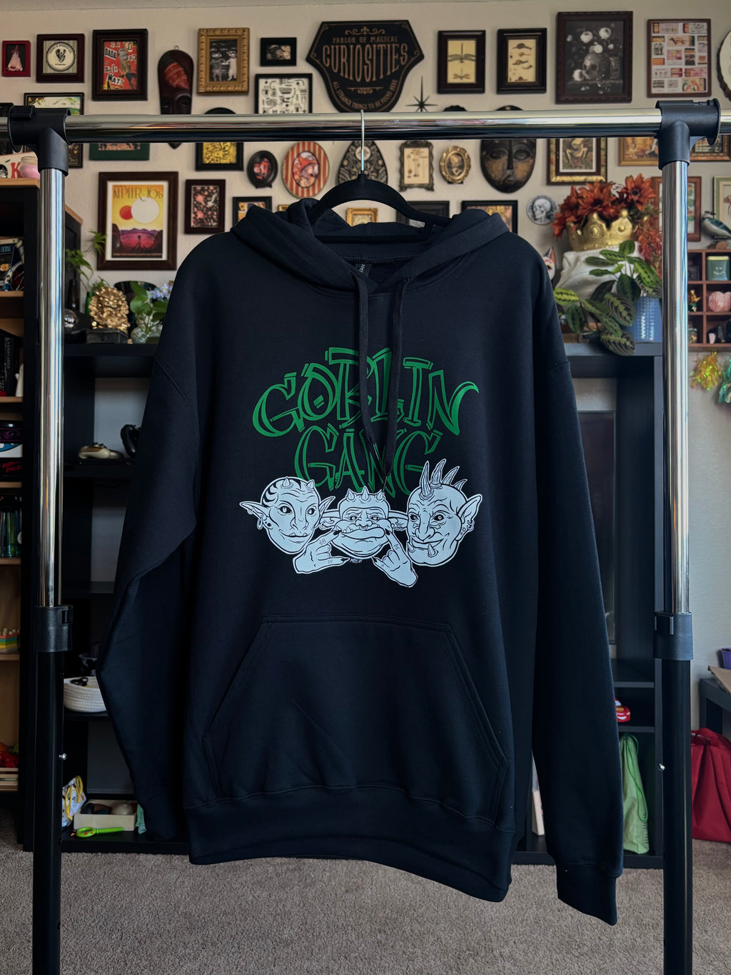black hoodie with "GOBLIN GANG" printed in green across the chest, and the faces of three goblins printed in black and white below, hanging on a rack