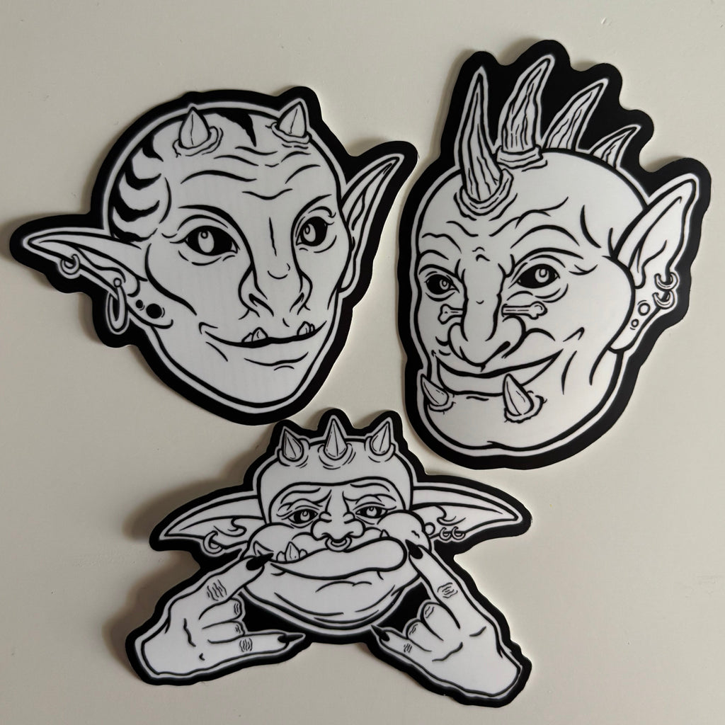 three different black and white stickers of goblin faces