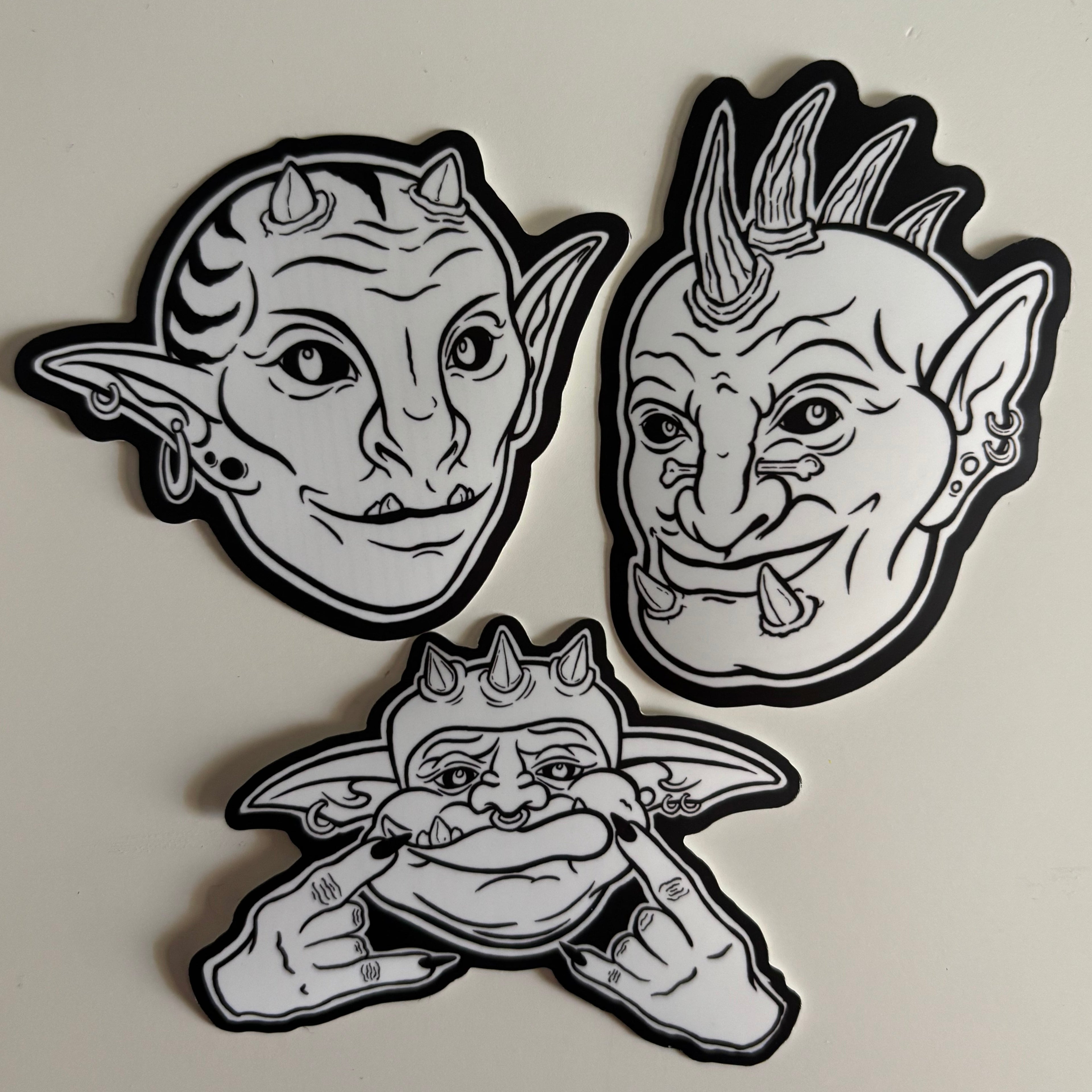 three different black and white stickers of goblin faces