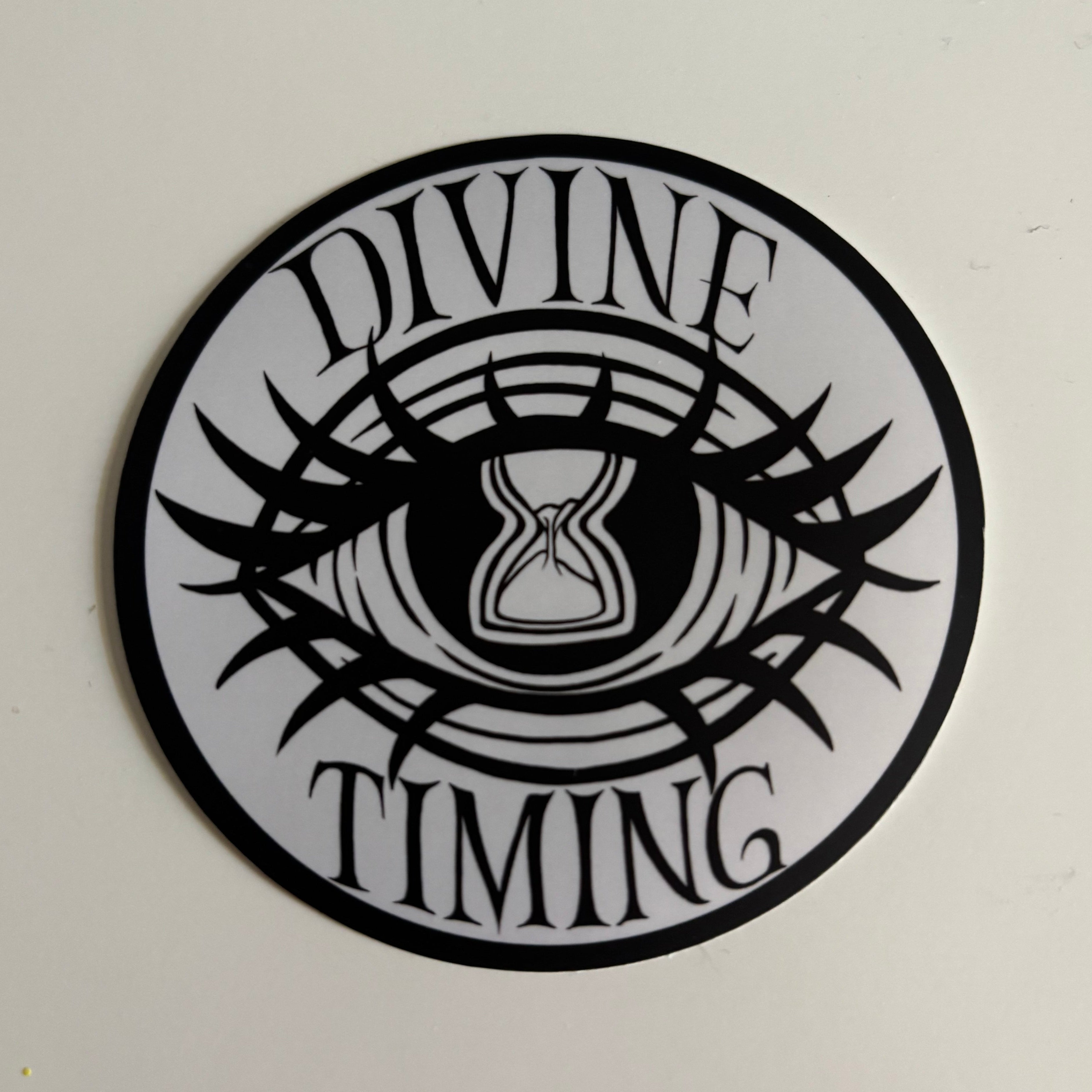 the Divine Timing Hourglass Eye logo printed as a black and white sticker