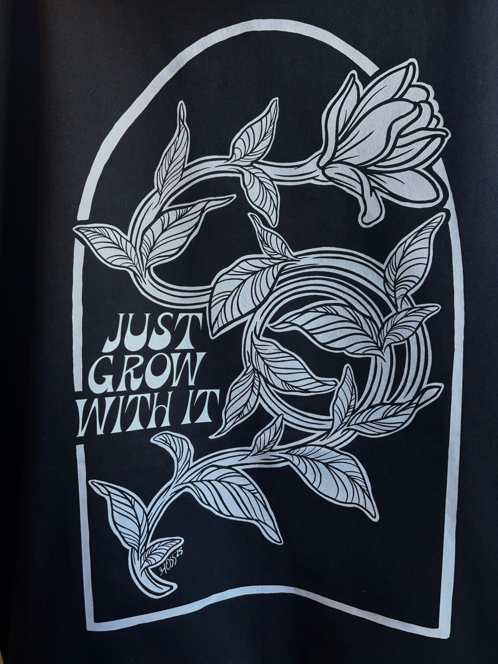 closeup look at the floral design on the back of a black hoodie, with "JUST GROW WITH IT" stamped next to it