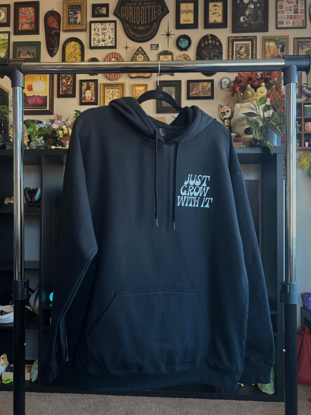 black hoodie with 'Just Grow With It' printed as a club patch, hanging on a rack