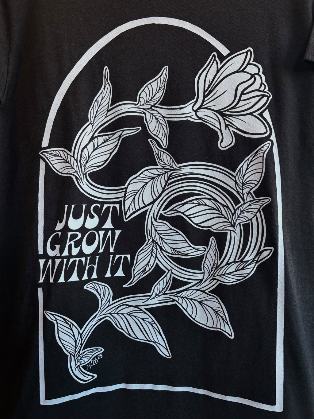 closeup look at the floral design on the back of a black t-shirt, with "JUST GROW WITH IT" stamped next to it