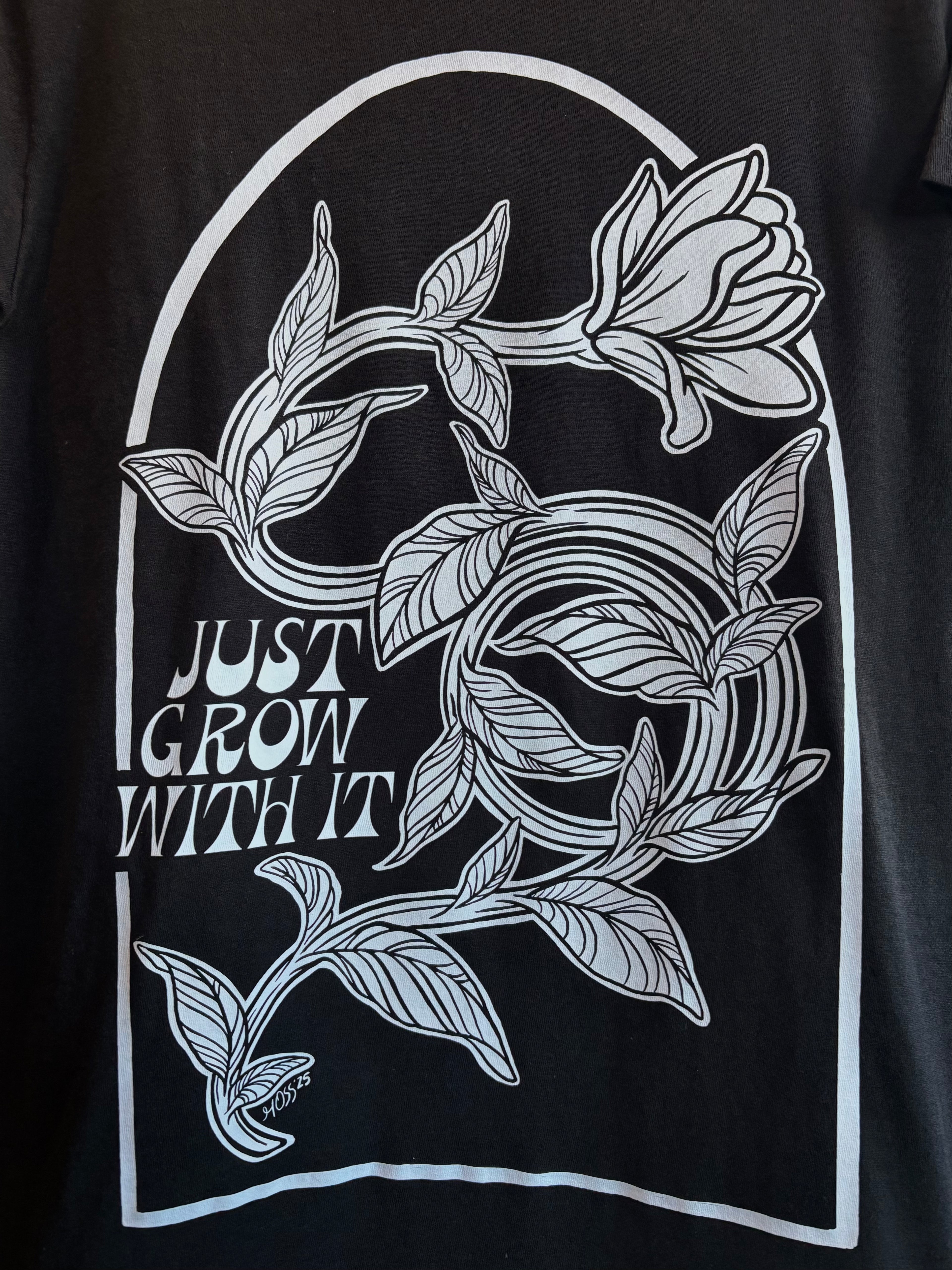 closeup look at the floral design on the back of a black t-shirt, with "JUST GROW WITH IT" stamped next to it