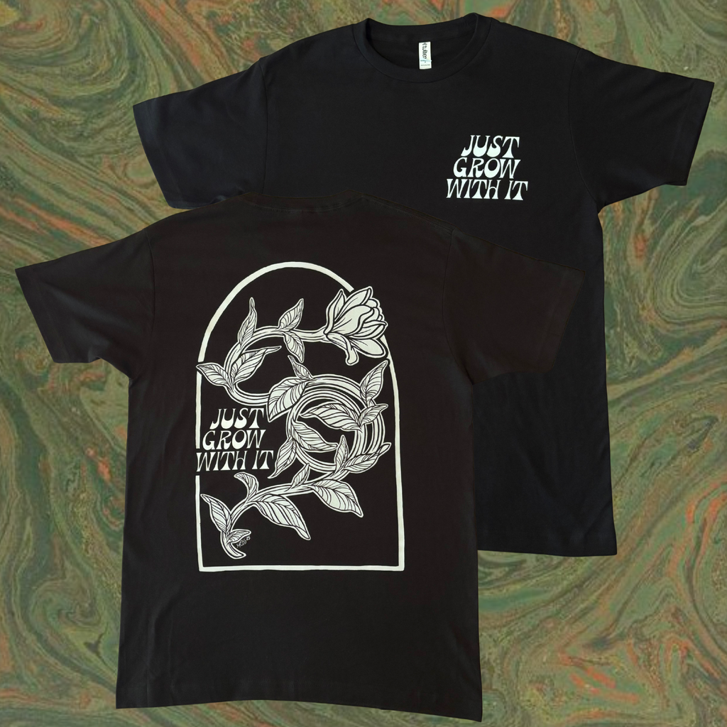 black t-shirt with white floral design on the back and text that says "Just Grow With It" 