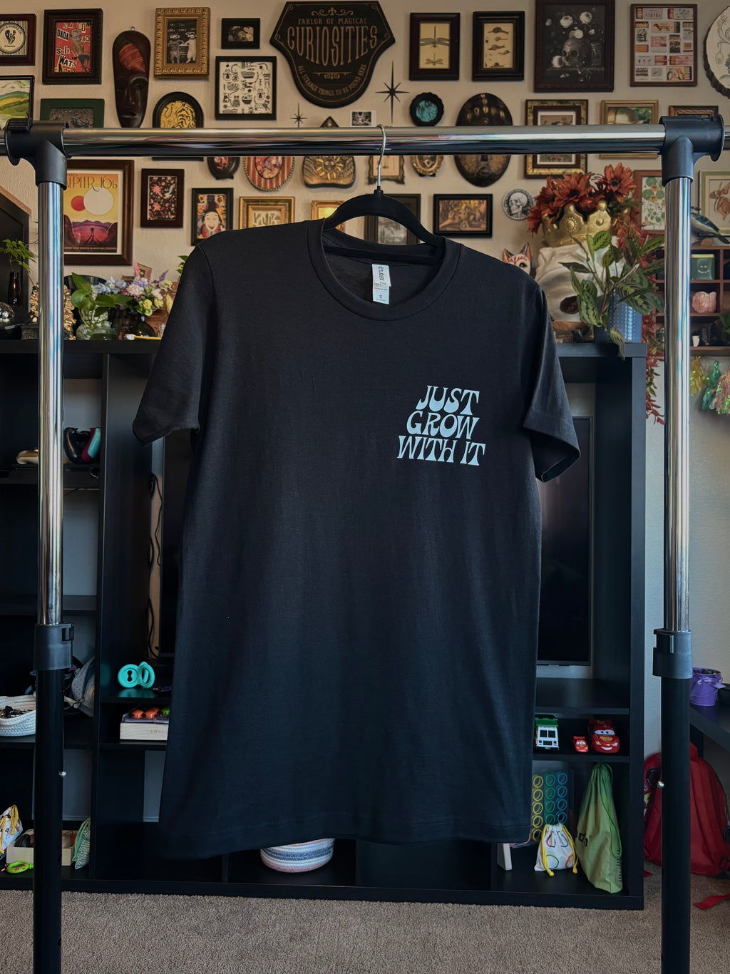black t-shirt with 'Just Grow With It' printed as a club patch, hanging on a rack