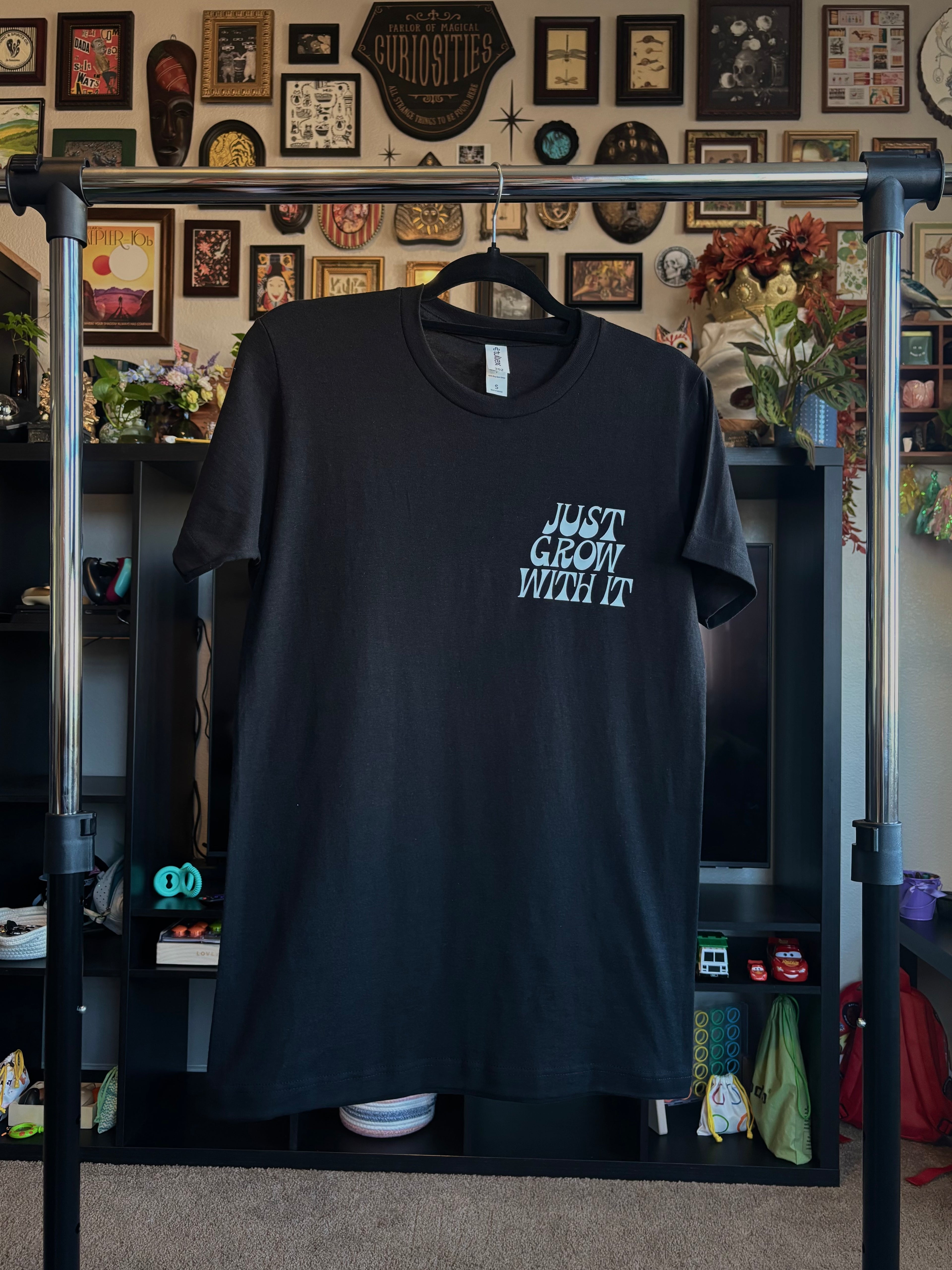 black t-shirt with 'Just Grow With It' printed as a club patch, hanging on a rack