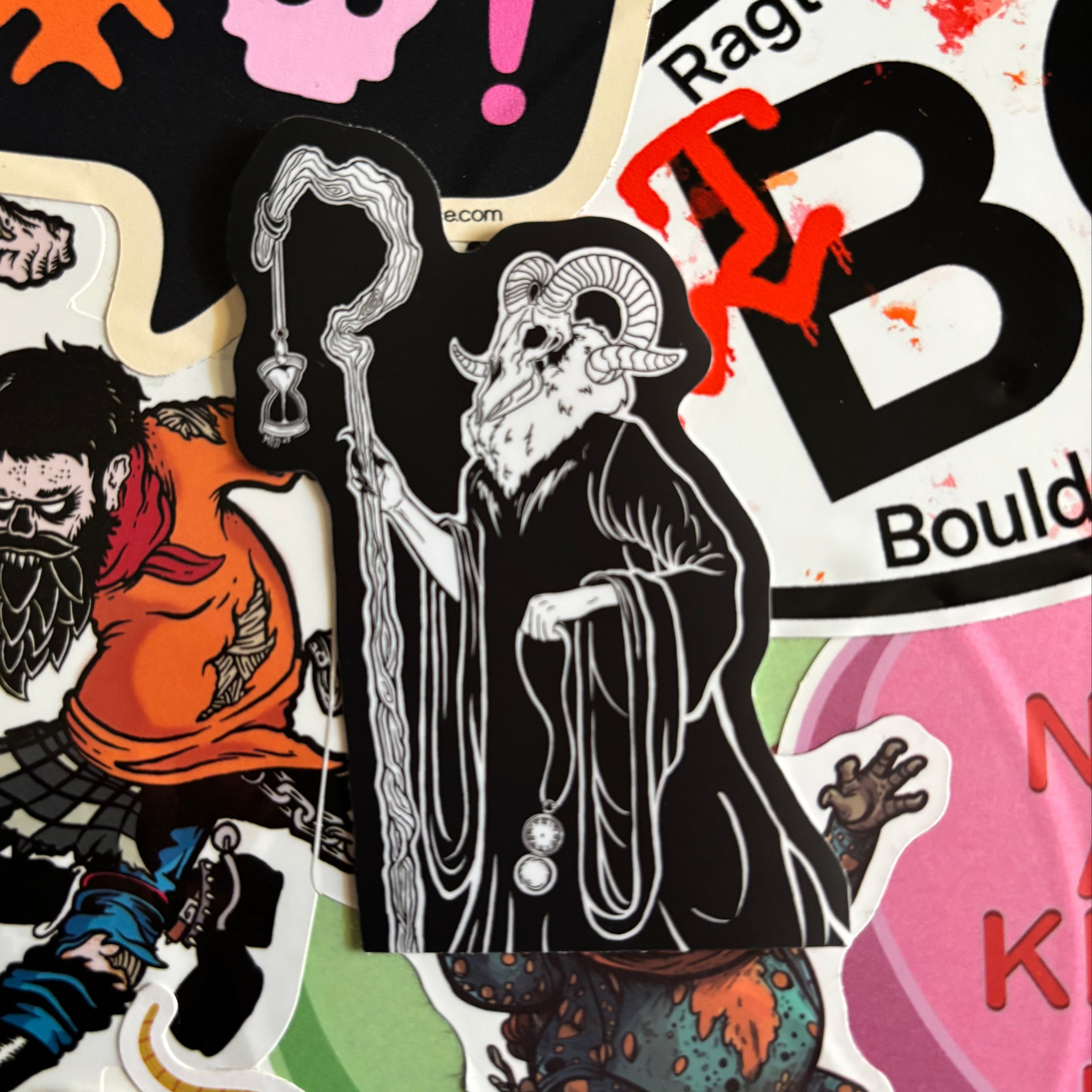 sticker of a spooky figure with a ram's head, holding a crooked staff, an hourglass, and a pocket watch.