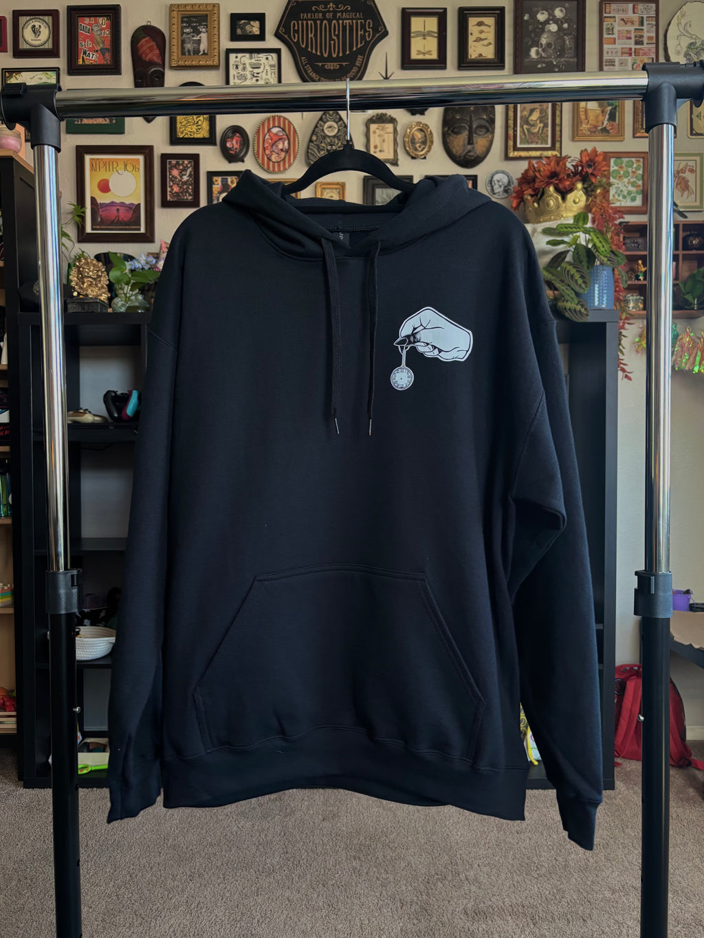 black hoodie with a club patch showing a spooky hand holding a small pocket watch