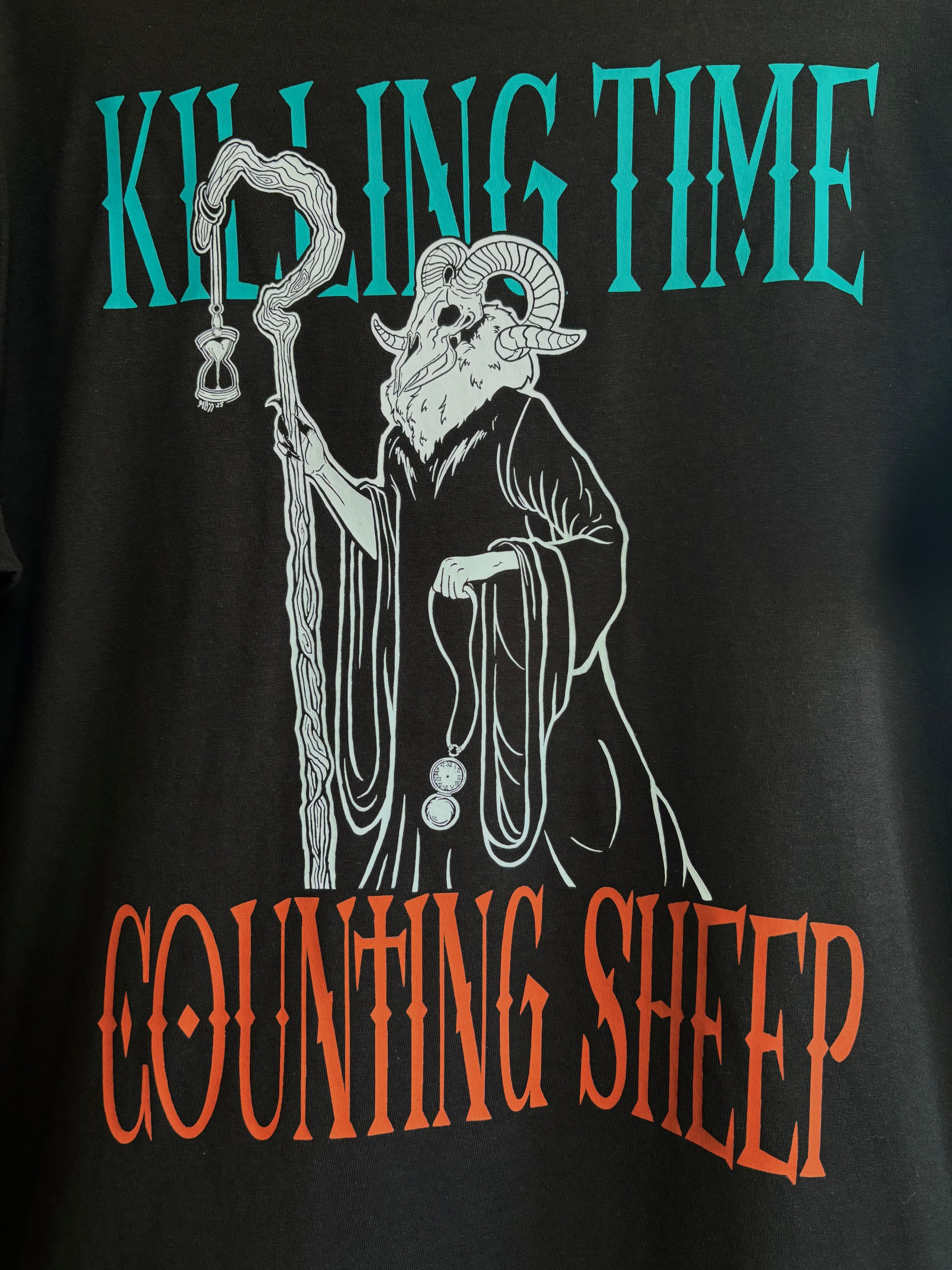 closeup image of the Killing Time design printed across the back of a black tee, showing the Keeper of Time surrounded by the text "Killing Time, Counting Sheep"