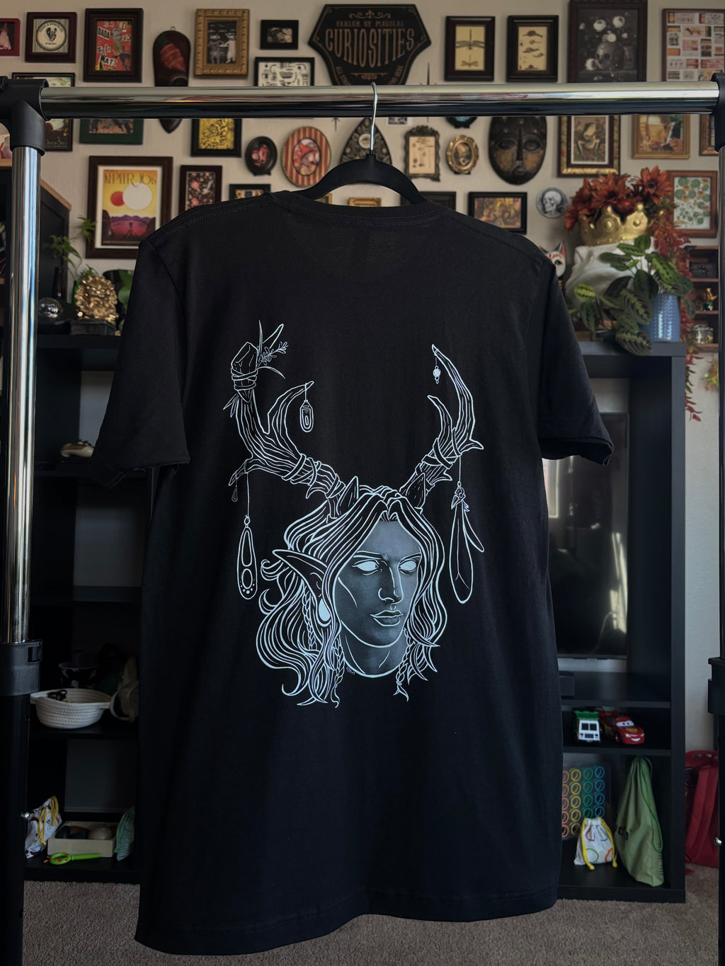 black tee hanging on a rack to display the King of the Forest, a Celtic inspired fae lord, printed across the back
