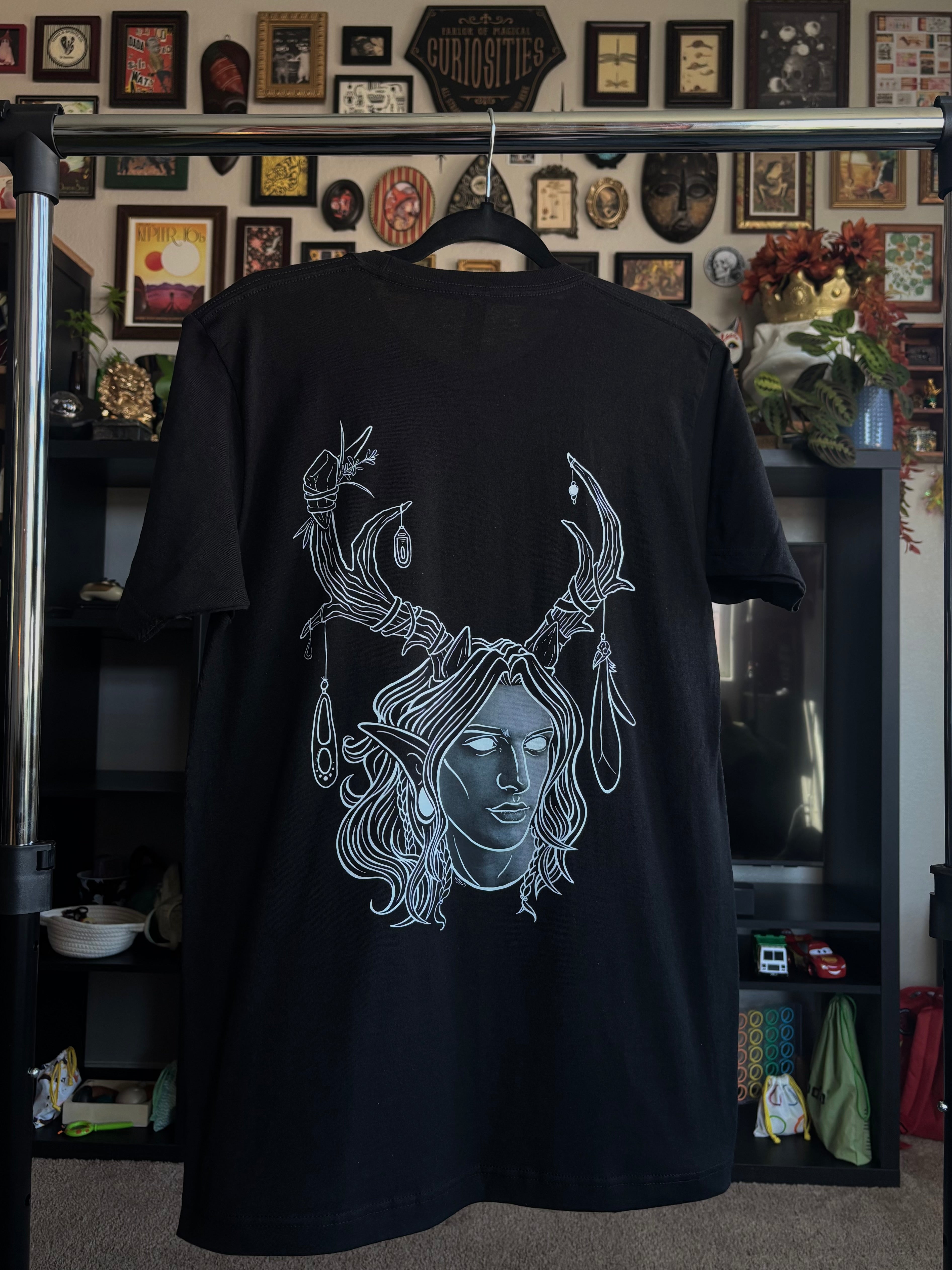 black tee hanging on a rack to display the King of the Forest, a Celtic inspired fae lord, printed across the back