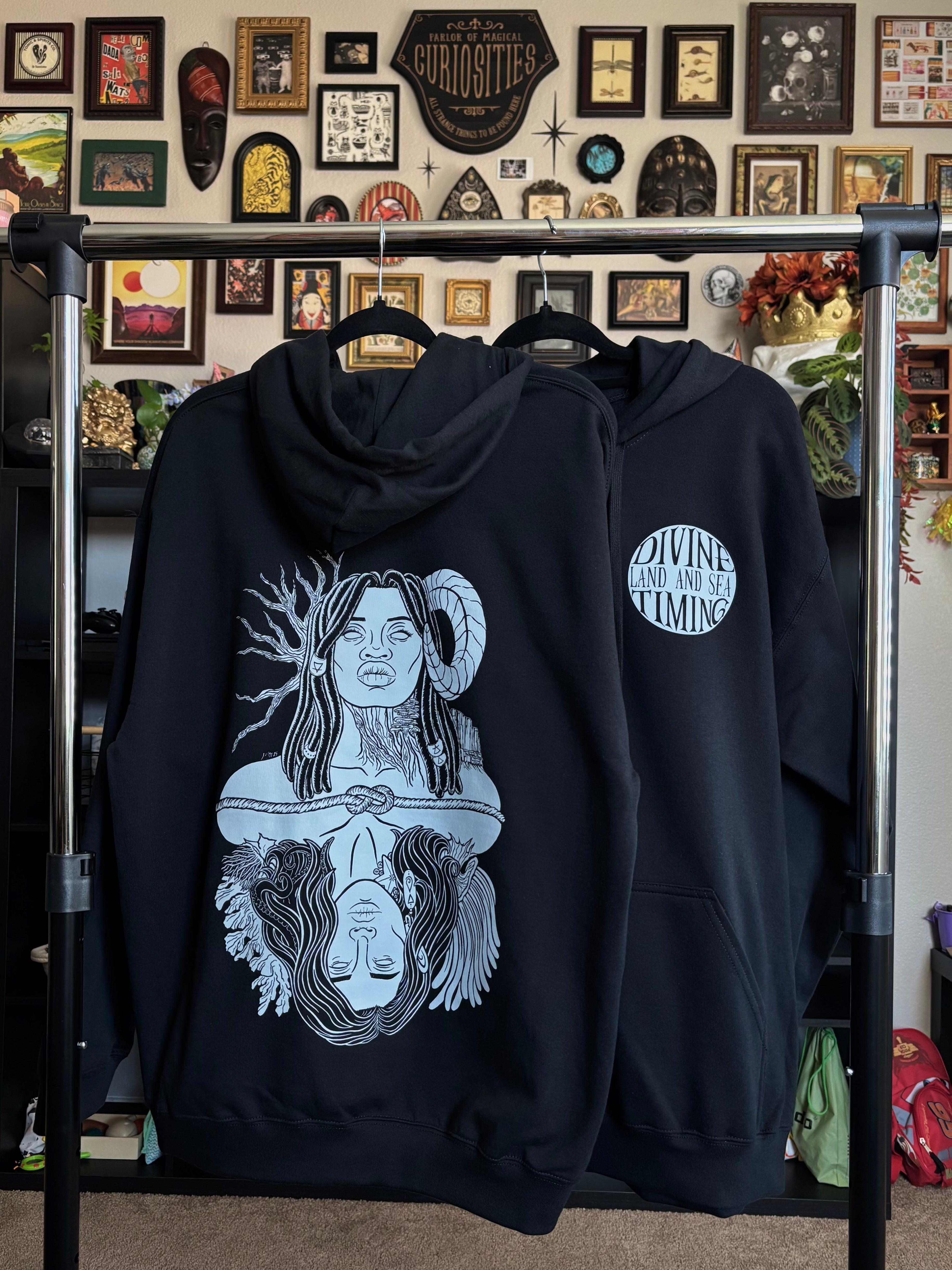 two black hoodies hanging on a rack to display the full back print of Gaia and Oceanus and the club patch on the front