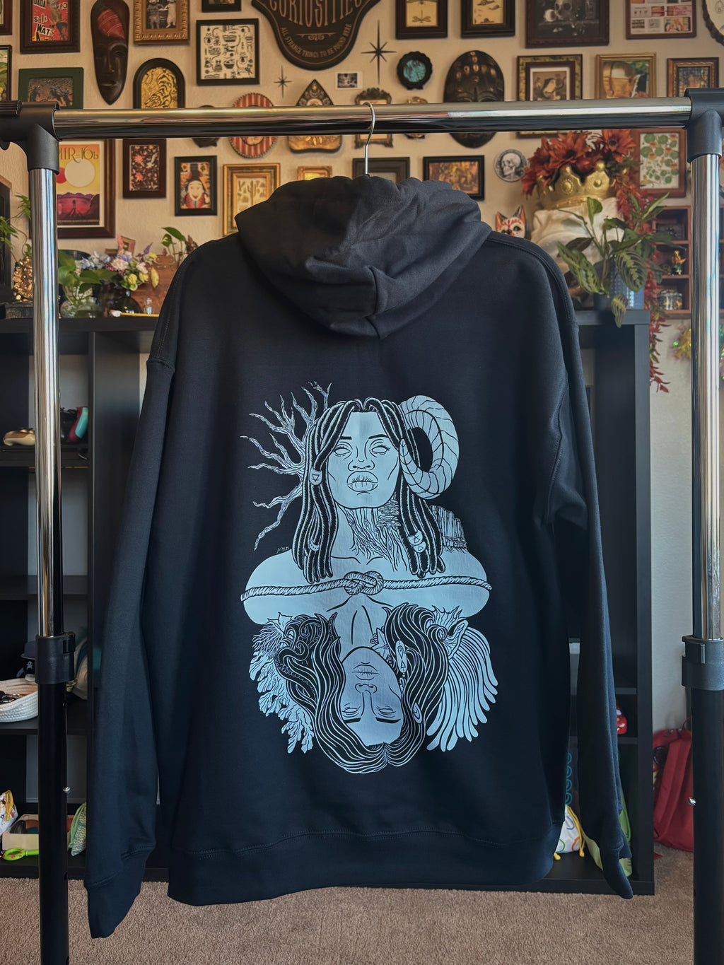 black hoodie hanging on a rack to show the full back print: a graphic design of Gaia, a powerful goddess adorned with beaded braids, a ram's horn, trees and mountains, who is connected to Oceanus, a god surrounded by coral and anemones with tentacles in his hair and a starfish and barnacles clinging to his neck