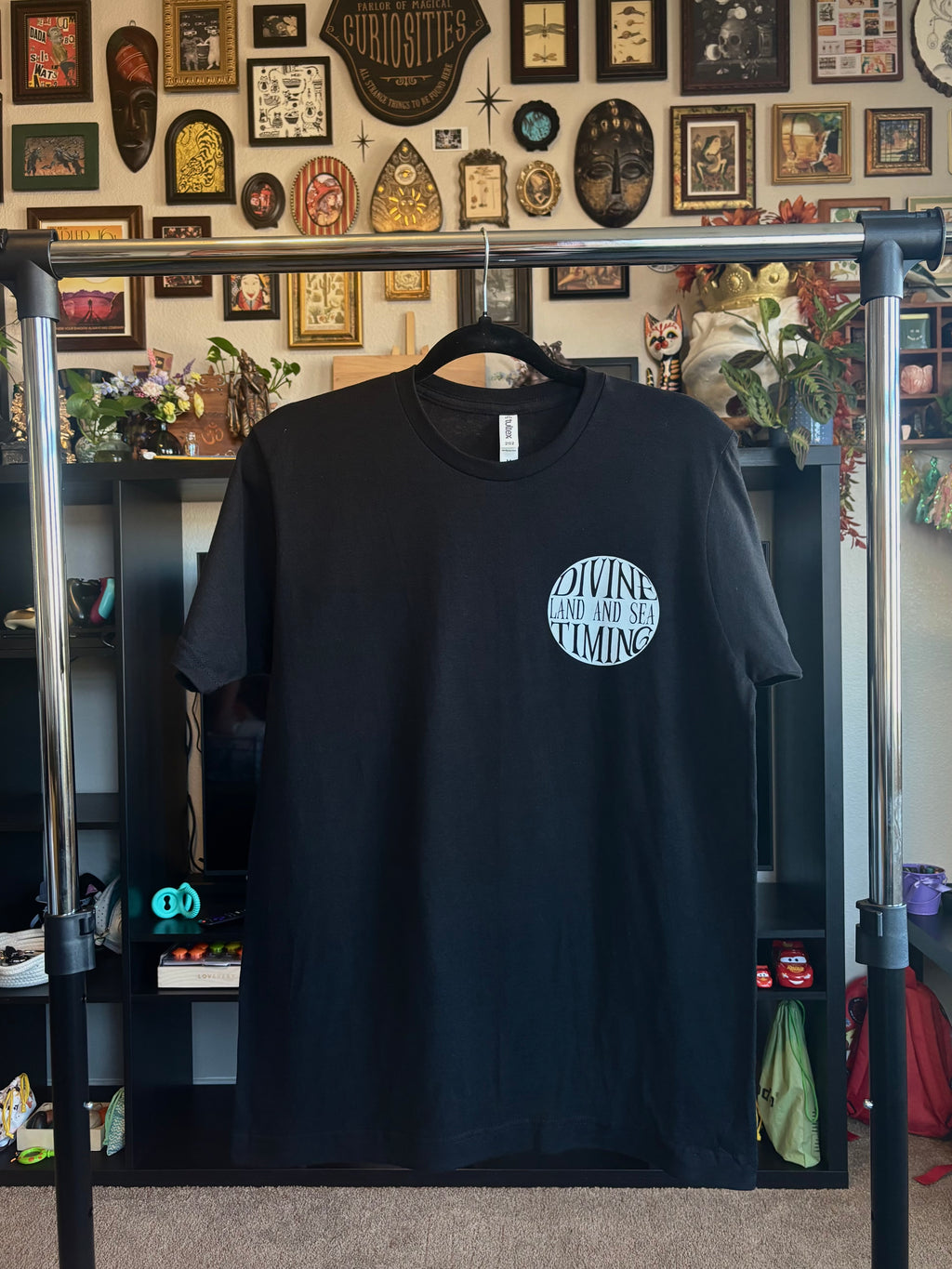 black tee hanging to show the front with the Divine Timing Land and Sea badge printed as a club patch