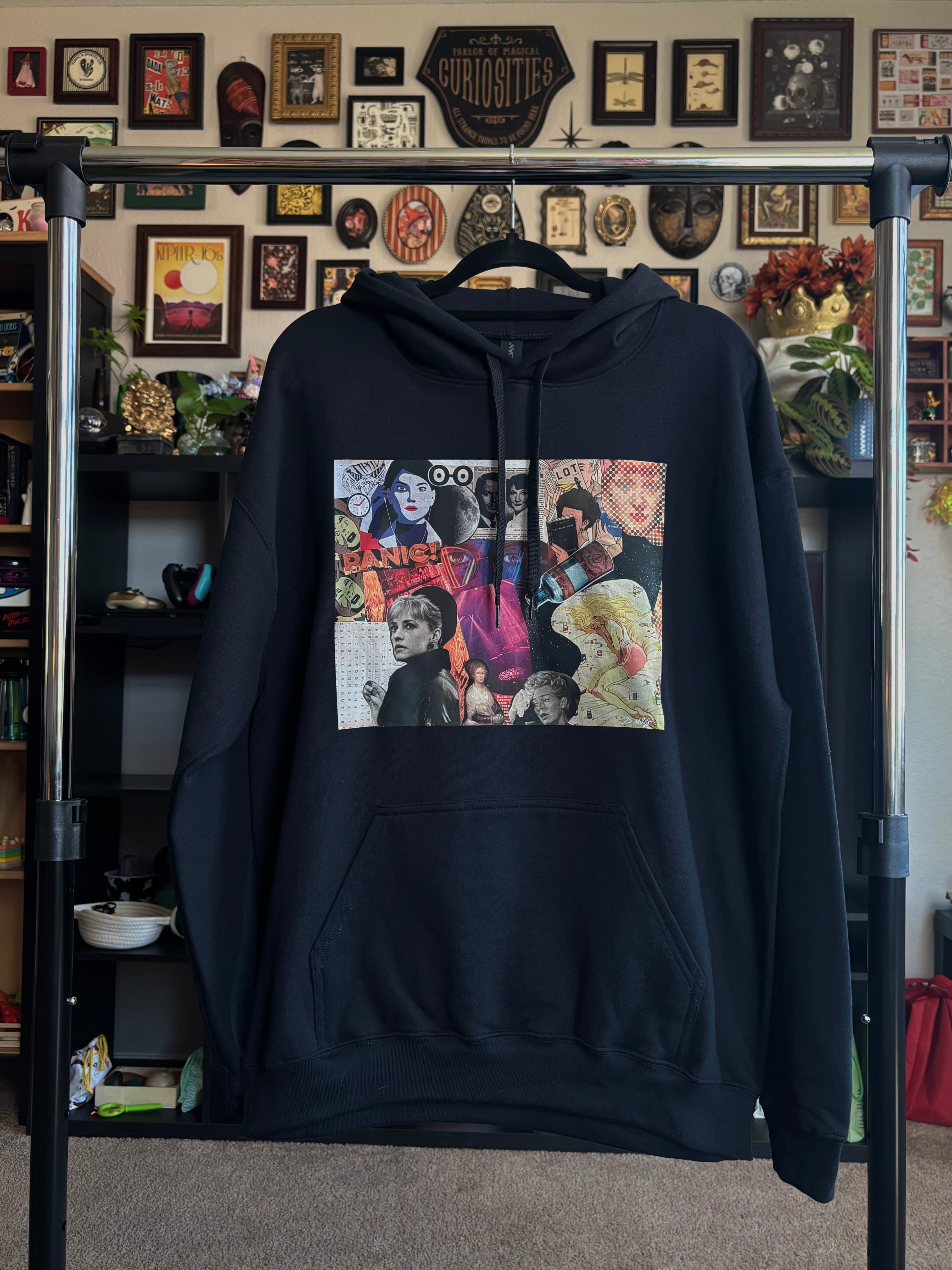 black hoodie with a colorful graphic design of the PANIC collage printed across the chest, shown hanging on a rack