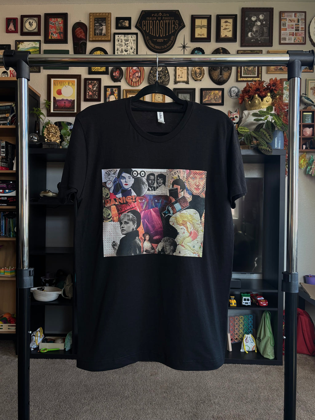 black tee with a colorful graphic design of the PANIC collage printed across the chest, shown hanging on a rack