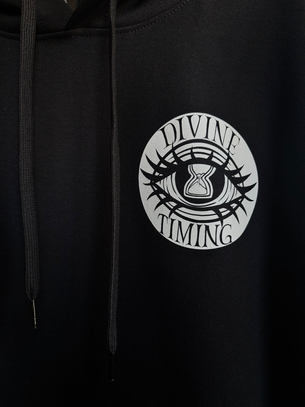 closeup look at the Divine Timing Hourglass Eye printed on the front of a black hoodie as a club patch